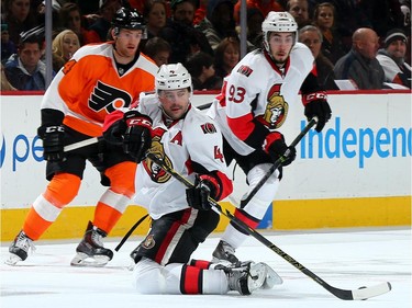 Chris Phillips #4 of the Ottawa Senators tries to keep the puck as teammate Mika Zibanejad #93 and Sean Couturier #14 of the Philadelphia Flyers stand by.