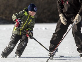 Rob Wallace, left, plays pond hockey with Jeff Hughes, right, and family on a frozen Mud Lake in Ottawa Friday, January 2, 2015. (Darren Brown/Ottawa Citizen)