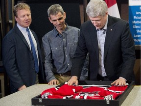 Prime Minister Stephen Harper, right, places a hockey jersey into a picture frame with store owner Joe Mancino, centre, and MP Rick Dykstra as they take part in a photo opportunity at Framecraft Ltd. in St. Catharines, Ont., on Thursday, January 22, 2015.