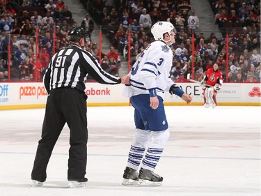 Dion Phaneuf #3 of the Toronto Maple Leafs is escorted to the players' bench by linesman Don Henderson after an altercation against Milan Michalek #9 of the Ottawa Senators.