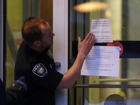 A police officer gets set to remove signs from front door at Ottawa Police headquarters on Elgin St. in Ottawa, Tuesday, February 17, 2015. Police received a threat around 2 p.m., prompting them to close all their stations to the public. A criminal investigation was launched and, later, around 5:30 p.m., all stations were re-opened. Mike Carroccetto / Ottawa Citizen