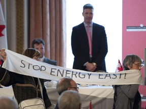 Standing on stage, Energy East Pipeline President François Poirier watches as protesters hold a banner in front of the podium during his speech to the Canadian Club of Canada during a luncheon in Ottawa, Monday, Feb. 2, 2015.