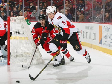 Cody Ceci #5 of the Ottawa Senators and Adam Henrique #14 of the New Jersey Devils skate towards a loose puck.