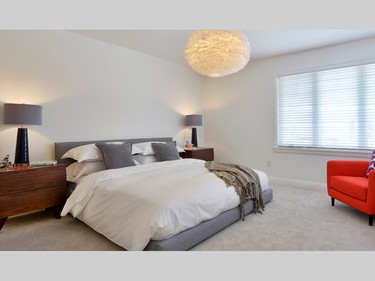 On the Minden's second level, a grey upholstered master bed is illuminated by a large, white, feathery light fixture.