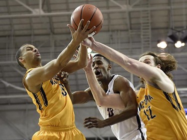 Carleton Ravens' Jean Emmanuel Pierre-Charles, centre, battle against Victoria Vikes' Jordan Charles (10) and Chris McLaughlin (12) for a rebound during first half CIS basketball action in Toronto on Saturday, March 14, 2015.