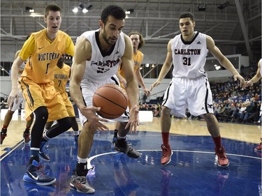 Carleton Ravens' Philip Scrubb (23) controls a loose ball as Victoria Vikes' Grant Sitton (0) and teammate Payen Boucard (31) look on during first half CIS basketball action in Toronto on Saturday, March 14, 2015.