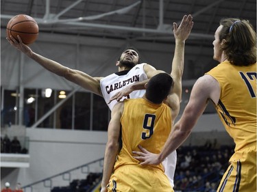 Carleton Ravens' Philip Scrubb (23) shoots as Victoria Vikes' Patrick Pilato (9) and Chris McLaughlin (12) defend  during first half CIS basketball action in Toronto on Saturday, March 14, 2015.