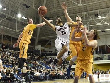 Carleton Ravens' Philip Scrubb (23) shoots as Victoria Vikes' Grant Sitton (0), Reiner Theil (4) and Chris McLaughlin (12) defend during second half CIS basketball action in Toronto on Saturday, March 14, 2015.