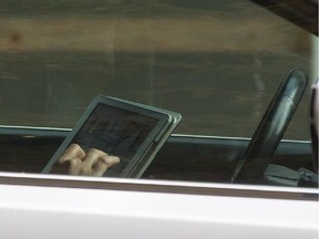 A woman uses an iPad while behind the wheel of a vehicle stopped in traffic at a red light