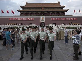 Paramilitary policemen march through a crowd at Tiananmen Square wiuth the Forbidden City in the background.