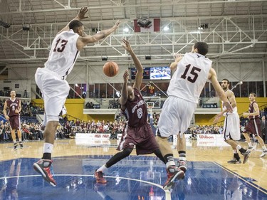 Ottawa Gee-Gees' Johnny Berhanemeskel (centre) loses possession as he his blocked by Carleton Ravens Jean Emmanuel Pierre-Charles (left) and Victor Raso (right) during first half CIS basketball final action in Toronto on Sunday, March 15, 2015.