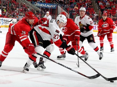 John-Michael Liles #26 of the Carolina Hurricanes reaches for the puck around Curtis Lazar #27 of the Ottawa Senators.