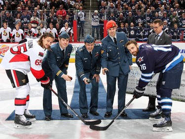 Erik Karlsson #65 of the Ottawa Senators and Andrew Ladd #16 of the Winnipeg Jets take part in the ceremonial puck drop with Canadian Armed Forces personnel during Canadian Armed Forces Appreciation Night.