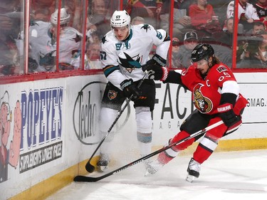 Erik Karlsson #65 of the Ottawa Senators and Tommy Wingels #57 of the San Jose Sharks dig for a loose puck along the boards.