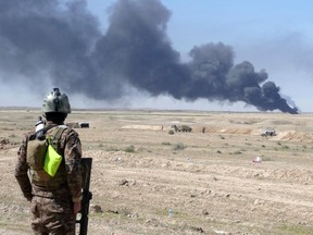 An Iraqi security forces member stands looking at smoke billowing from the Ajeel oil field located 35 km northeast of Tikrit on March 11, 2015, after it was reportedly set on fire by the Islamic State jihadist (IS) group to provide cover from air strikes during the military operation by Iraqi pro-government forces to retake the city.