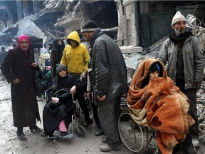 In this Feb. 4, 2014, file photo released by the Syrian official news agency SANA, Palestinian residents of the besieged refugee camp of Yarmouk wait at the gate of the camp to receive aid supplies from the United Nations on the southern edge of the Syrian capital, Damascus.