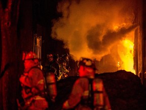 Firefighters attempt to control a structure fire as flames spill out of the alleyway behind the Beaver's Mug cafe and Silver Scissors Hair in the Glebe on Bank Street in Ottawa on Thursday, April 9, 2015.