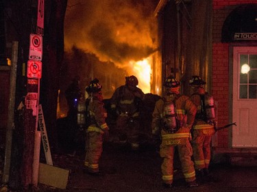Firefighters attempt to control a structure fire as flames spill out of the alleyway behind the Beaver's Mug cafe and Silver Scissors Hair in the Glebe on Bank Street in Ottawa on Thursday, April 9, 2015.