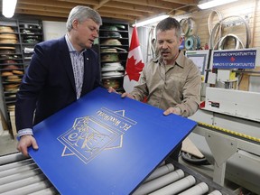 Prime Minister Stephen Harper speaks with Rick Mostert, president of FC Woodworks Inc., as the use an Edgebender to put an edge on a piece of wood Thursday, April 23, 2015. Harper also spoke to supporters about a tax cut to small business included in the Economic Action Plan 2015 during a press conference at FC Woodworks in Winnipeg.