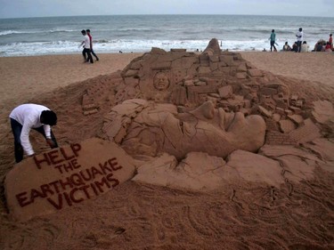 Indian sand artist Sudarsan Pattnaik puts the final touches on his sand sculpture to commemorate the earthquake in Nepal, on a beach in Puri, some 65 kilometers from Bhubaneswar on April 25, 2015.  A massive 7.8 magnitude earthquake killed hundreds of people April 25 as it ripped through large parts of Nepal, toppling office blocks and towers in Kathmandu and triggering a deadly avalanche that hit Everest base camp.