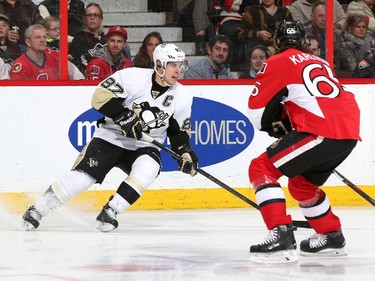 Sidney Crosby #87 of the Pittsburgh Penguins controls the puck, looking to make a pass, against Erik Karlsson #65 of the Ottawa Senators.