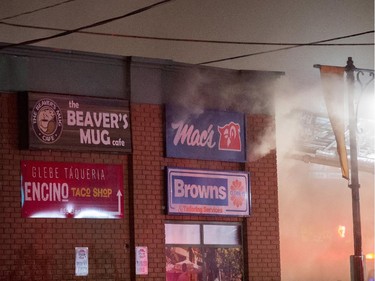 Smoke spills from the wall of a Glebe business unit as firefighters attempt to control a structure fire at the Beaver's Mug cafe and Silver Scissors Hair  in the Glebe on Bank Street in Ottawa on Thursday, April 9, 2015.