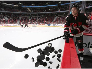 Mark Stone #61 of the Ottawa Senators knocks the pucks off the rink board ledge during warmups.
