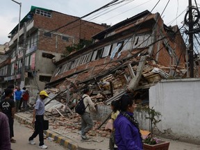 Nepalese people walk past a collapsed bullding in Kathmandu after an earthquake on April 25, 2015. A massive 7.8 magnitude earthquake killed hundreds of people April 25 as it ripped through large parts of Nepal, toppling office blocks and towers in Kathmandu and triggering a deadly avalanche that hit Everest base camp.