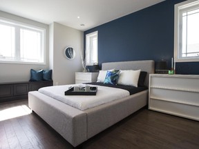 In the model, the grey, black and white-themed master bedroom is punched up with a deep blue accent wall, a panelled window seat with storage, and a grey fabric headboard for the bed.