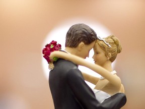 Figurines of a bride and a groom sit atop a wedding cake.
