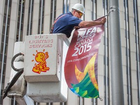Hector DiMillo hangs a FIFA banner on a lamp post outside city hall along Elgin St.