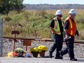 Transportation Safety Board investigators walk past a makeshift memorial on the Transitway near Fallowfield Station in Barrhaven on Sept. 28, 2013.