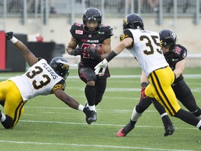 Ottawa Redblacks defensive back John Stevenson (46) carries the football while being defended by Hamilton Tiger-Cats linebacker Frédéric Plesius (33) and Hamilton Tiger-Cats defensive back Mike Daly (35) during the first half of their CFL game in Hamilton on Monday.