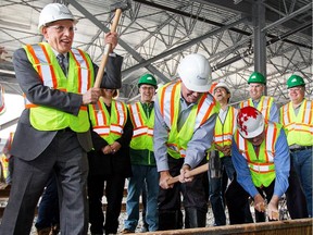 Ontario Transport Minister Bob Chiarelli (L) playfully mocks pounding Mayor Jim Watson (C) in the noggin while Royal Galipeau (R) concentrates on hitting the spike during a ceremony marking the laying of the first official rail track of the O-Train Confederation Line light rail transit project at the Belfast Yard maintenance and storage facility. Photo taken on June 12.