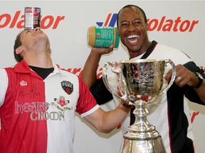 Ottawa Redblacks quarterback, Henry Burris (right), and Ottawa Fury defender, Mason Trafford, wound up with cans of soup and peanut butter jars in front of the Grey Cup at the Ottawa Food Bank Thursday, July 16, 2015. Both teams are asking fans to bring a non perishable food item or money donation to their games this weekend in the hopes of raising 55,000 pounds of food for the Ottawa Food Bank.