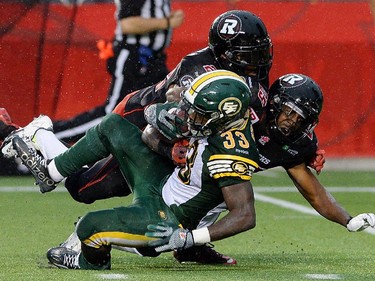 The Ottawa Redblacks' Brandon McDonald, top, and teammate Brandyn Thompson tackle the Edmonton Eskimos' Shakir Bell during the second quarter.