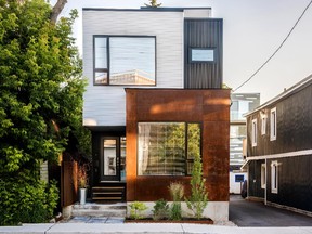 The house appears as a series of articulated boxes. The lower box is clad in sandblasted raw steel that has already turned a rich mottled orange. Softer, grey-stained western white cedar and shiny black corrugated metal panels on the remaining boxes provide striking contrasts while an orange-rusted steel grid helps frame the covered entrance.