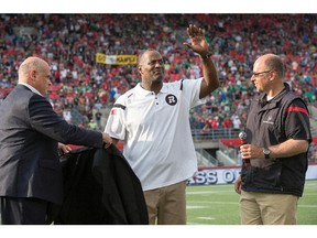 Leroy Blugh acknowledges the crowd's applause as he is helped on with his Hall of Fame jacket by Mark DeNobile, left, with Redblacks GM Marcel Desjardins looking on at halftime on Sunday, Aug. 30, 2015.