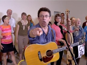 Ottawa folksinger Tony Turner wrote and performed the song Harperman with help from Ann Downey on bass and the Crowd of Well Wishers choir, June 12, 2015 (screen capture from video)