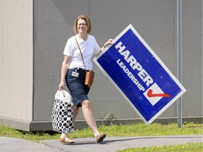 A woman holding a sign supporting Conservative Leader Stephen Harper walks to her car on Parliament Hill  on Sunday. A City of Ottawa bylaw prohibits such signs in the municipality until at least Aug. 20.