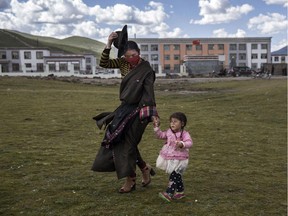 A Tibetan woman holds on to her hat in strong winds as she walks her daughter home from a Chinese government school in a resettlement community on July 23, 2015 on the Tibetan Plateau in Yushu County, Qinghai, China. Tibetan nomads face many challenges to their traditional way of life including political pressures, forced resettlement by China's government, climate change and rapid modernization.