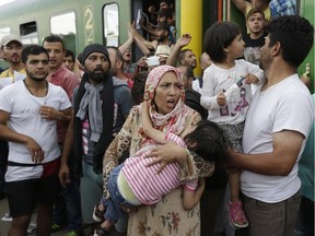 A woman carrying a child stands outside a train with migrants that was stopped in Bicske, Hungary, Thursday, Sept. 3, 2015. More than 150,000 migrants have reached Hungary this year, most coming through the southern border with Serbia. Many apply for asylum but quickly try to leave for richer EU countries.