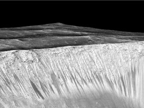 A handout image made available by NASA on September 27, 2015, dark narrow streaks called recurring slope lineae emanating out of the walls of Garni crater on Mars. The dark streaks here are up to few hundred meters in length. They are hypothesized to be formed by flow of briny liquid water on Mars.