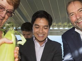 NDP leader Tom Mulcair, right, alongside NDP candidate for the riding of Brossard-Saint Lambert, Hoang Mai, shucks corn during a federal election campaign stop at a seniors residence in Brossard, Que., on Friday.