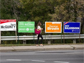 A woman walks past a group of election signs on Bank St opposite South Keys Shopping Centre in Ottawa South.