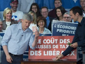 Conservative Leader Stephen Harper holds up a handful of cash to illustrate proposed Liberal tax hikes during a campaign event in Trois-Rivieres, Que.