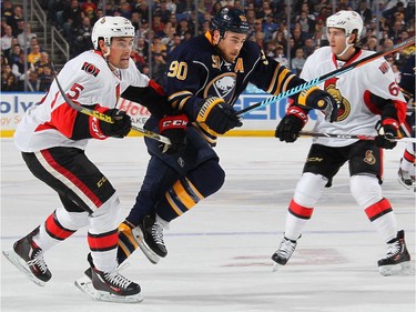 Ryan O'Reilly #90 of the Buffalo Sabres battles Cody Ceci #5 and Mike Hoffman #68 of the Ottawa Senators while pursuing the puck.