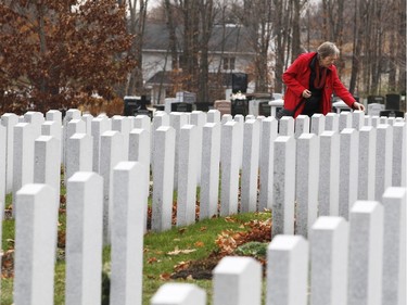 A woman lays a poppy atop a tombstone after the Remembrance Day ceremony at the National Military Cemetery on the grounds of the Beechwood Cemetery Wednesday November 11, 2015.