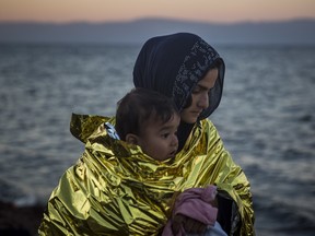 A woman wearing a thermal blanket holds her child on a beach on the Greek island of Lesbos shortly after crossing the Aegean sea on a dinghy from the Turkey's coast with other refugees and migrants on Friday, Nov. 20, 2015. Most nations along Europe's refugee corridor, except Greece, abruptly shut their borders Thursday to those not coming from war-torn countries such as Syria, Afghanistan or Iraq, leaving thousands desperately seeking a better life in the continent stranded at Balkan border crossings.