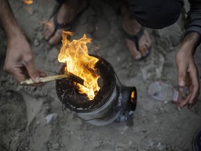 In this Wednesday, Nov. 4, 2015 photo, a migrant makes a fire for making tea inside the migrants camp near Calais, northern France. Many of the estimated 6,000 residents spend hours queuing for six-minute showers and one daily meal at a government-funded facility on the camp's Atlantic-facing edge. Elsewhere, campers stand in mud to collect cold water from batteries of hose-fed taps and burn tree branches to cook and boil water, turning the air acrid with smoke.